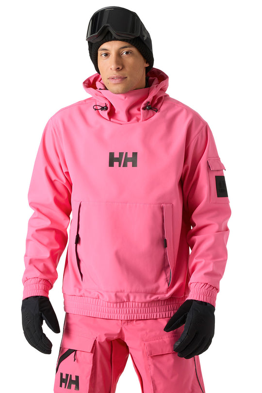 A man wearing a bright pink Helly Hansen snow jacket and matching snow pants, with black gloves, a black beanie, and black ski goggles, photographed against a plain white background.