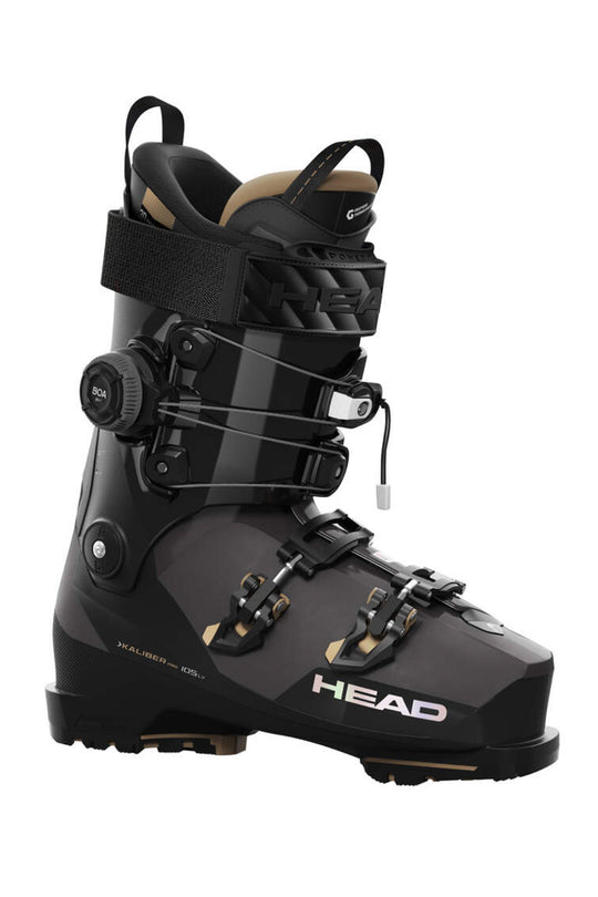 A single ski boot from the brand HEAD, shown in a side profile view against a solid white background. The boot is primarily black with dark gray panels and features tan accents on the inner lining and buckle details.