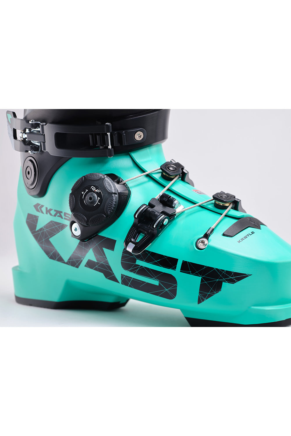 A close-up of a Kastle ski boot in a vibrant turquoise color with black accents, including the brand logo, buckles, and straps, set against a light gray background.