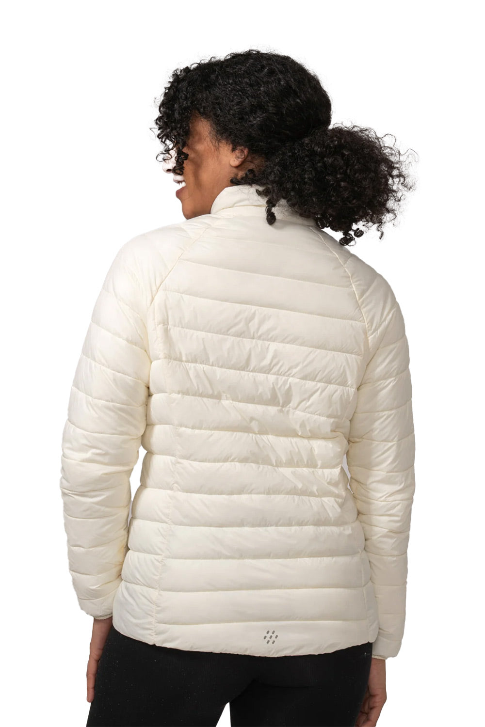 A woman viewed from the back wearing a cream-colored, horizontally quilted puffer jacket and black pants against a plain white background.