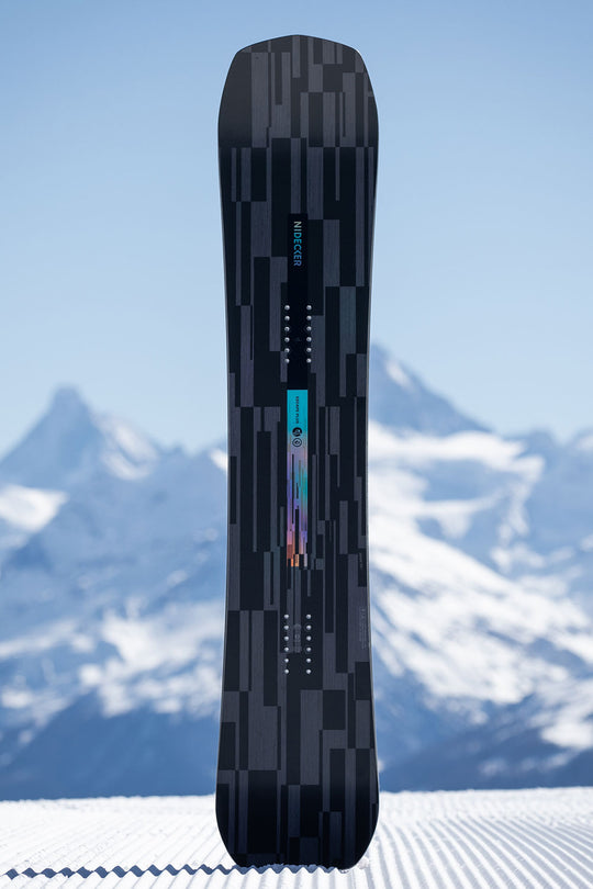 Black snowboard with a geometric pattern against a snowy mountain background