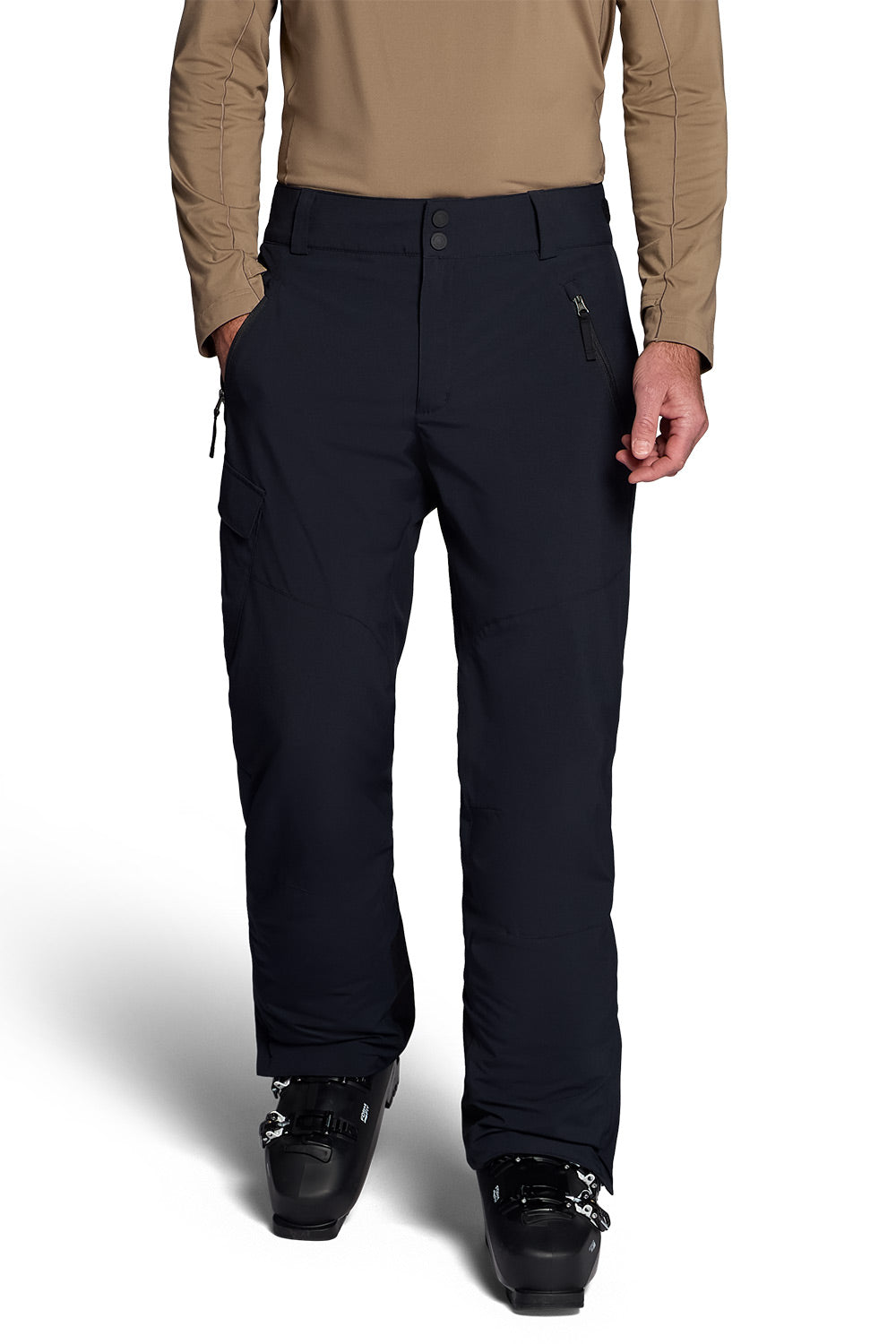 A person wearing black ski pants with a tan long-sleeve top and black ski boots, shown from the chest down against a white studio background.