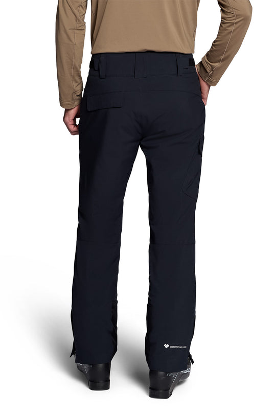 Rear view of a person wearing black pants with a tan long-sleeve top, standing against a white studio background.