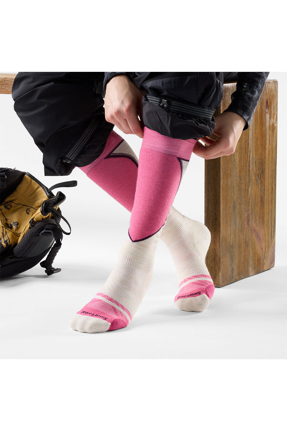 Person wearing pink socks with a black jacket and backpack on a white background