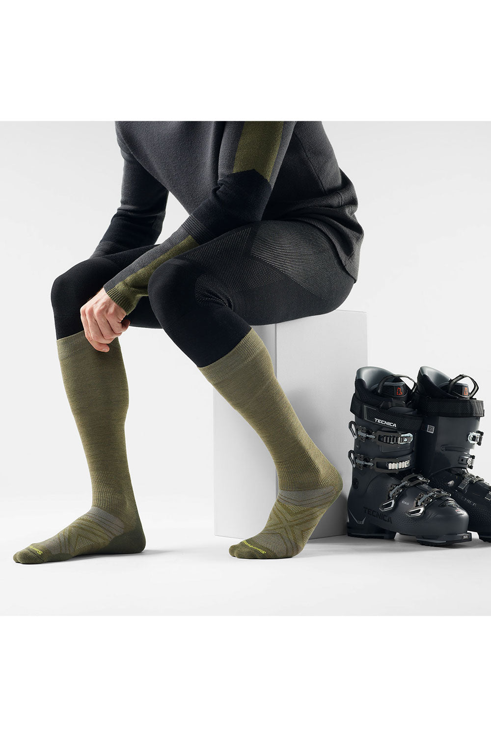 Person wearing green socks with black ski boots on a white background