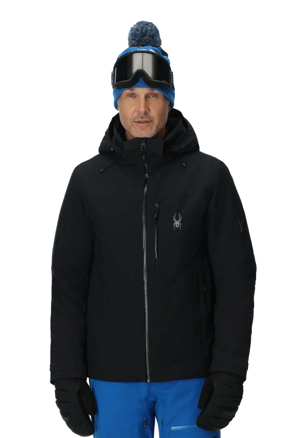 Person wearing a black jacket with a brand logo, blue pants, and a blue beanie with goggles on a white background