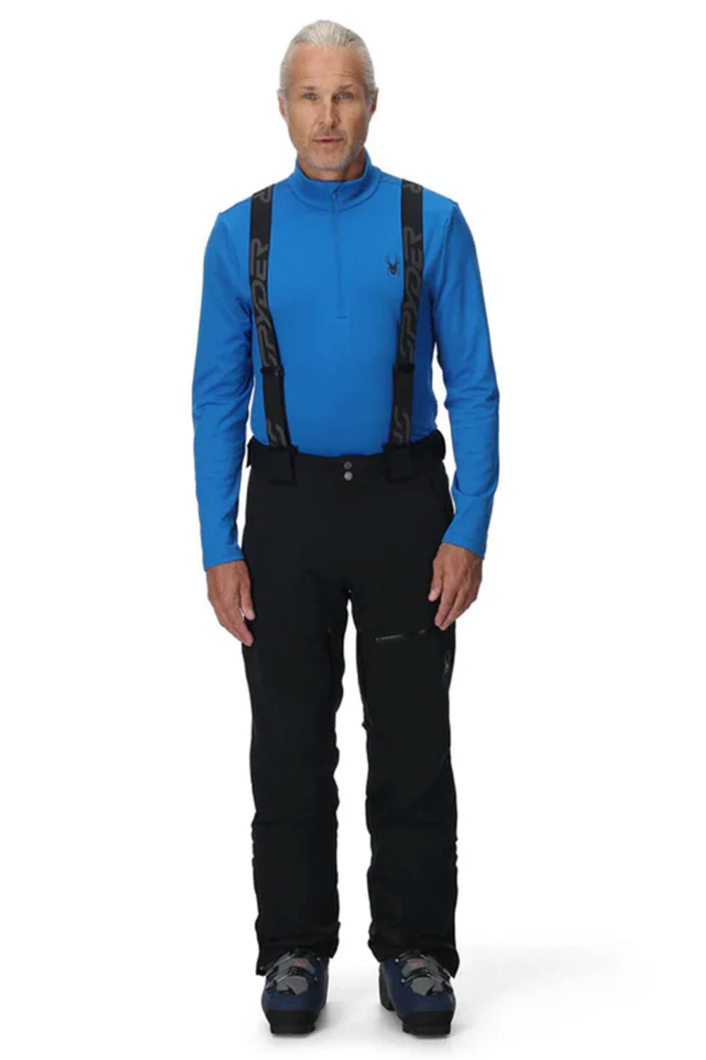 Man wearing a blue jacket and black pants with suspenders on a white background