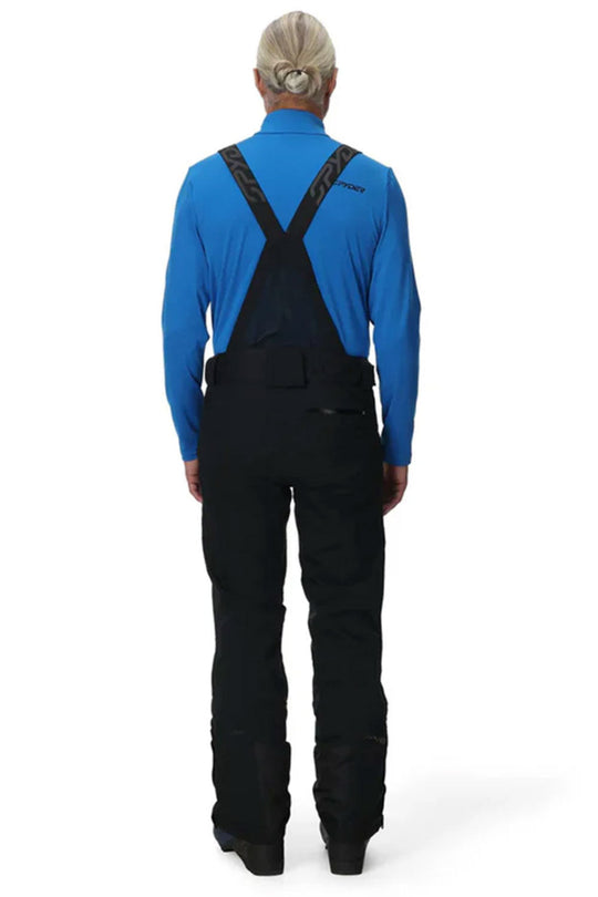 Person wearing a blue shirt and black pants with suspenders on a white background
