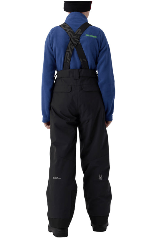 Back view of a person wearing Spyder snow pants and a blue long-sleeve top with black suspenders against a white background.