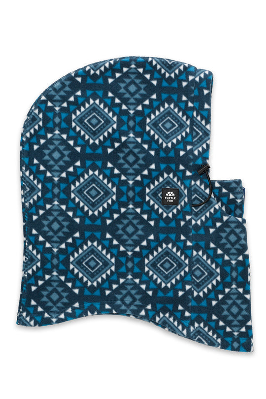 A hooded face mask with a blue and white geometric pattern, featuring a small black logo patch on the side.