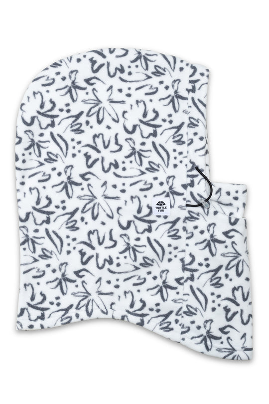 A white fleece balaclava or neck warmer with a black hand-drawn floral and abstract pattern, featuring a small black logo on the front and a black drawstring.