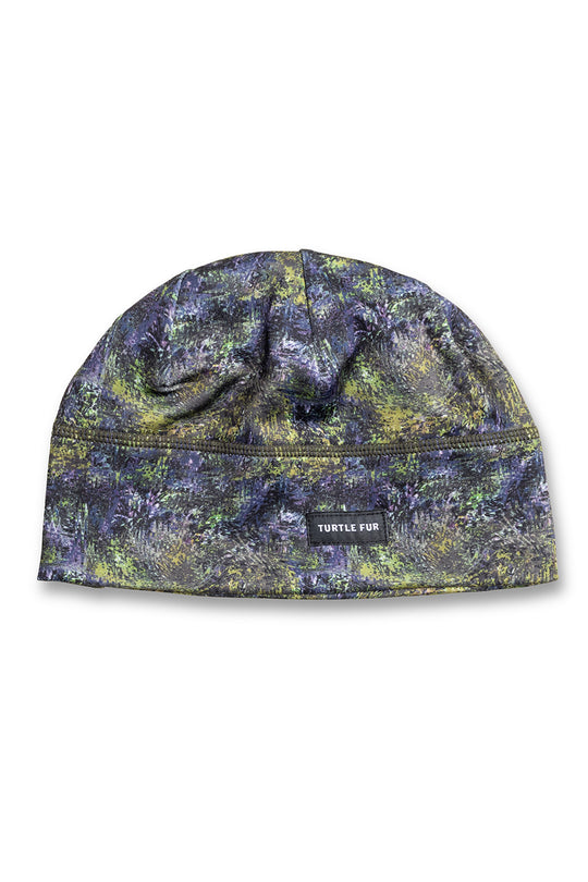 A flat-brim beanie hat featuring a textured, mottled camouflage pattern in dark blue, green, and yellow. A small black brand label reading 'TURTLE FUR' is stitched on the front center seam.