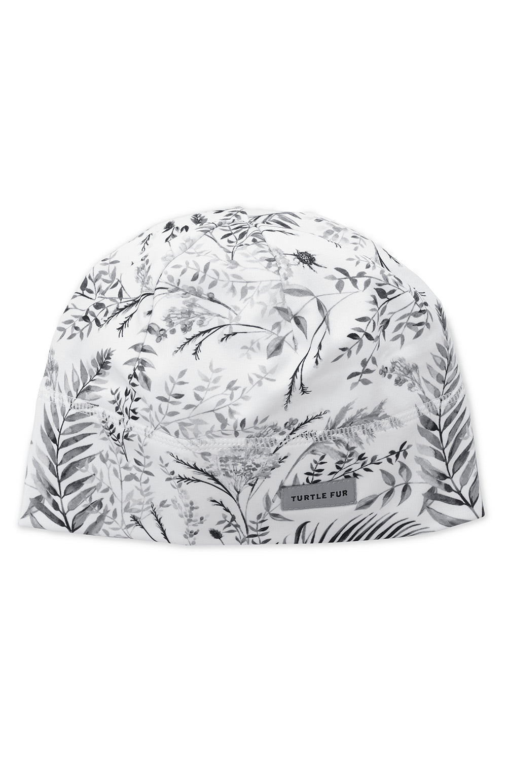 A white knit cap with a black botanical leaf pattern, featuring a small rectangular brand label that reads 'TURTLE FUR'.