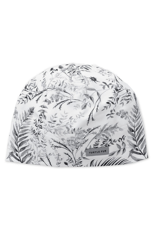 A white knit cap with a black botanical leaf pattern, featuring a small rectangular brand label that reads 'TURTLE FUR'.