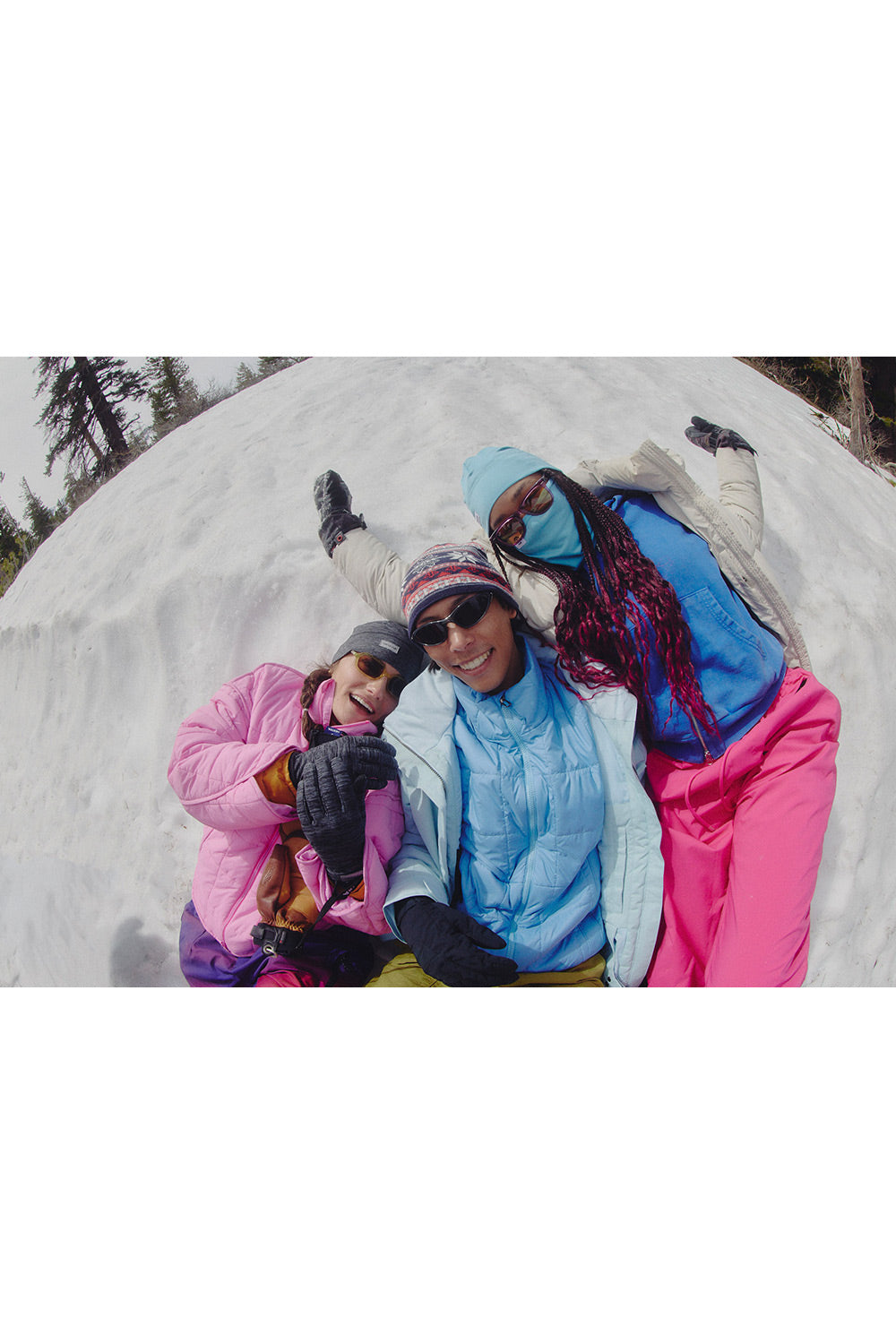 Three people in colorful ski jackets and snow pants posing together on a snowy slope, viewed from a low angle with a wide, slightly distorted perspective.