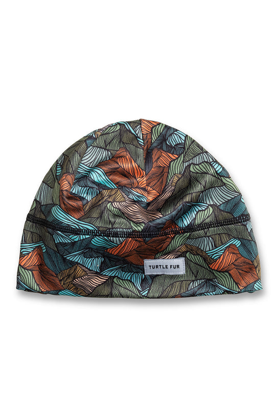A beanie hat with a colorful abstract pattern of teal, orange, and gray shapes on a dark background, featuring a small white 'TURTLE FUR' brand label.