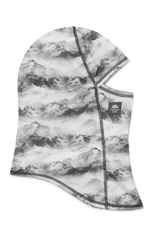 A one-piece hooded neck warmer or face mask with a black and white mountain range pattern, featuring a small black brand patch on the side.