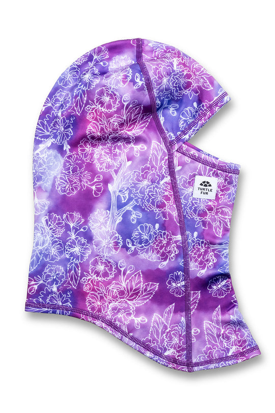 A purple and blue floral hooded face mask with a white floral pattern, featuring a small white brand label on the side.