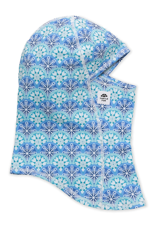 A hooded neck warmer or balaclava with an all-over snowflake pattern in shades of blue, teal, and white, featuring a small white brand label on the side.