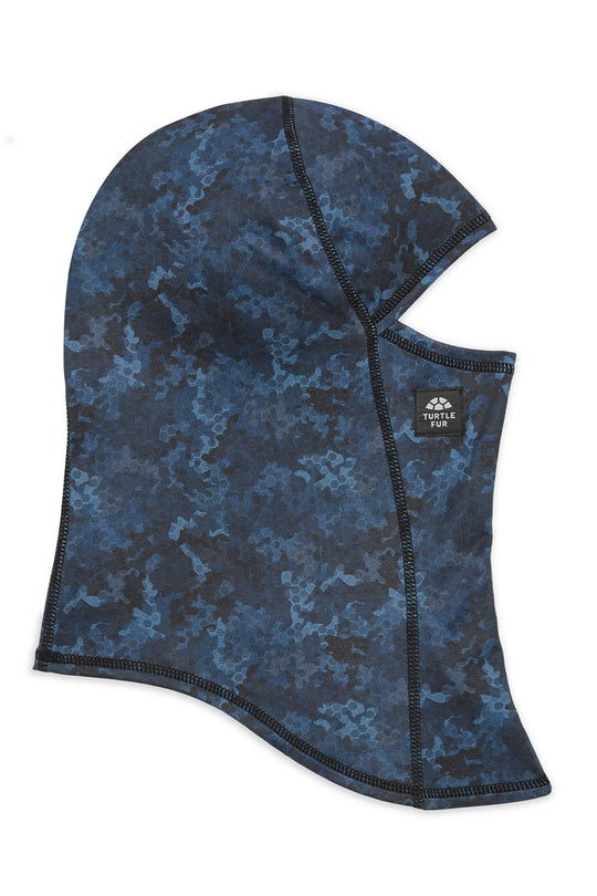 A blue and black camouflage balaclava face covering with a small black brand patch on the side, shown against a plain white background.
