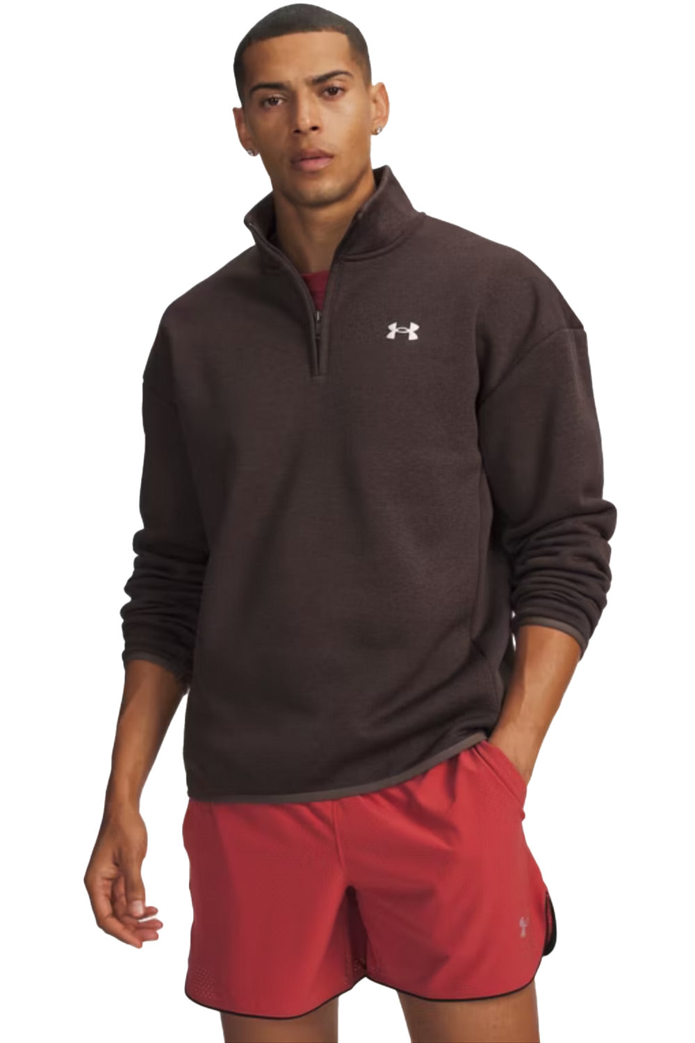 A man wearing a dark brown Under Armour quarter-zip pullover and red athletic shorts, standing against a plain white background.