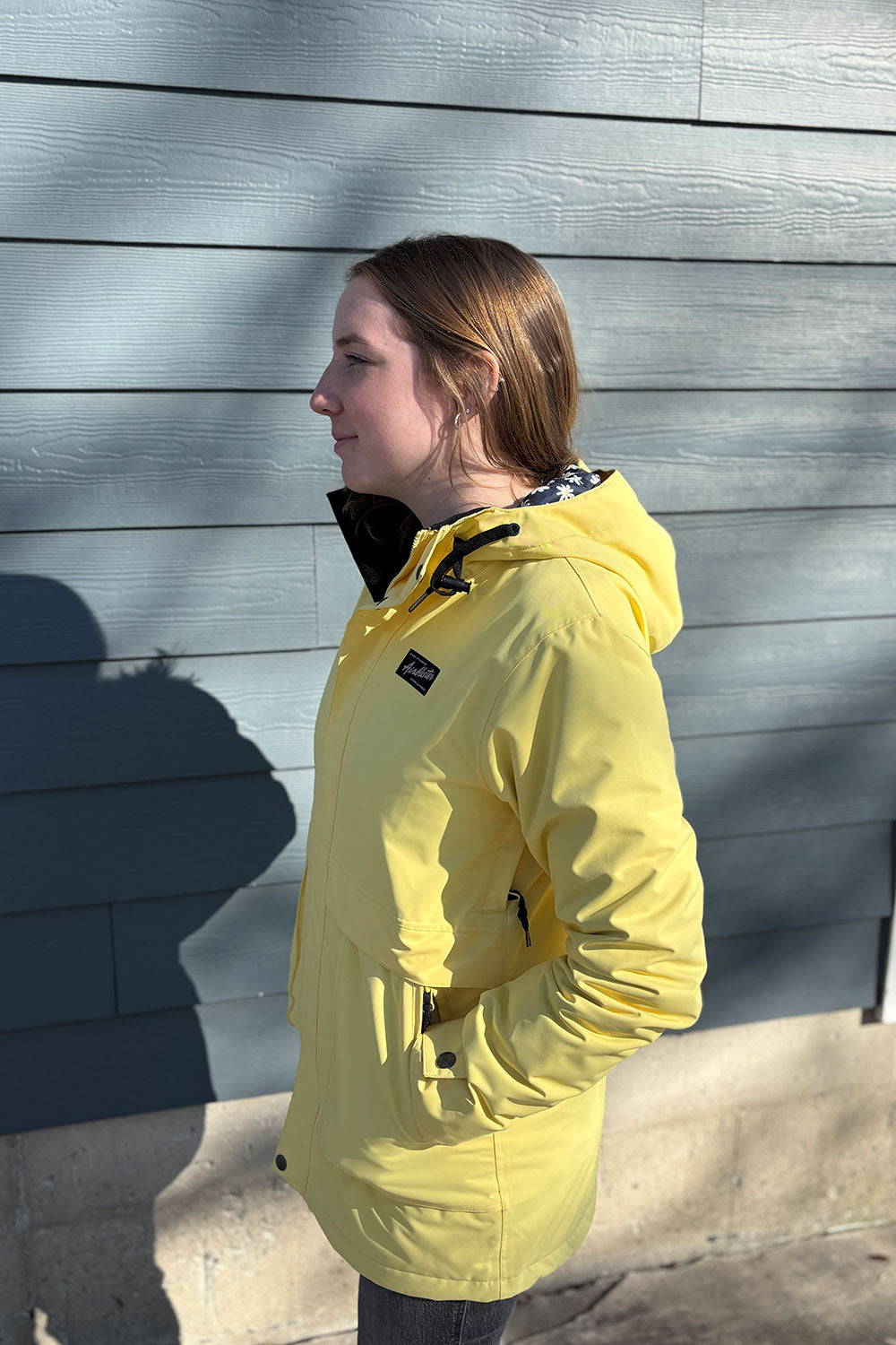 Person wearing a yellow jacket standing against a gray wooden wall.