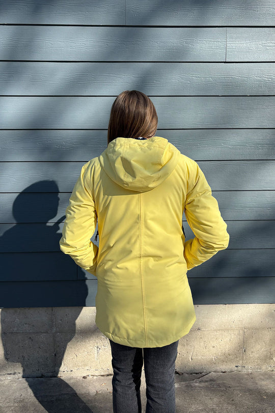 Person wearing a yellow jacket standing against a gray wall.