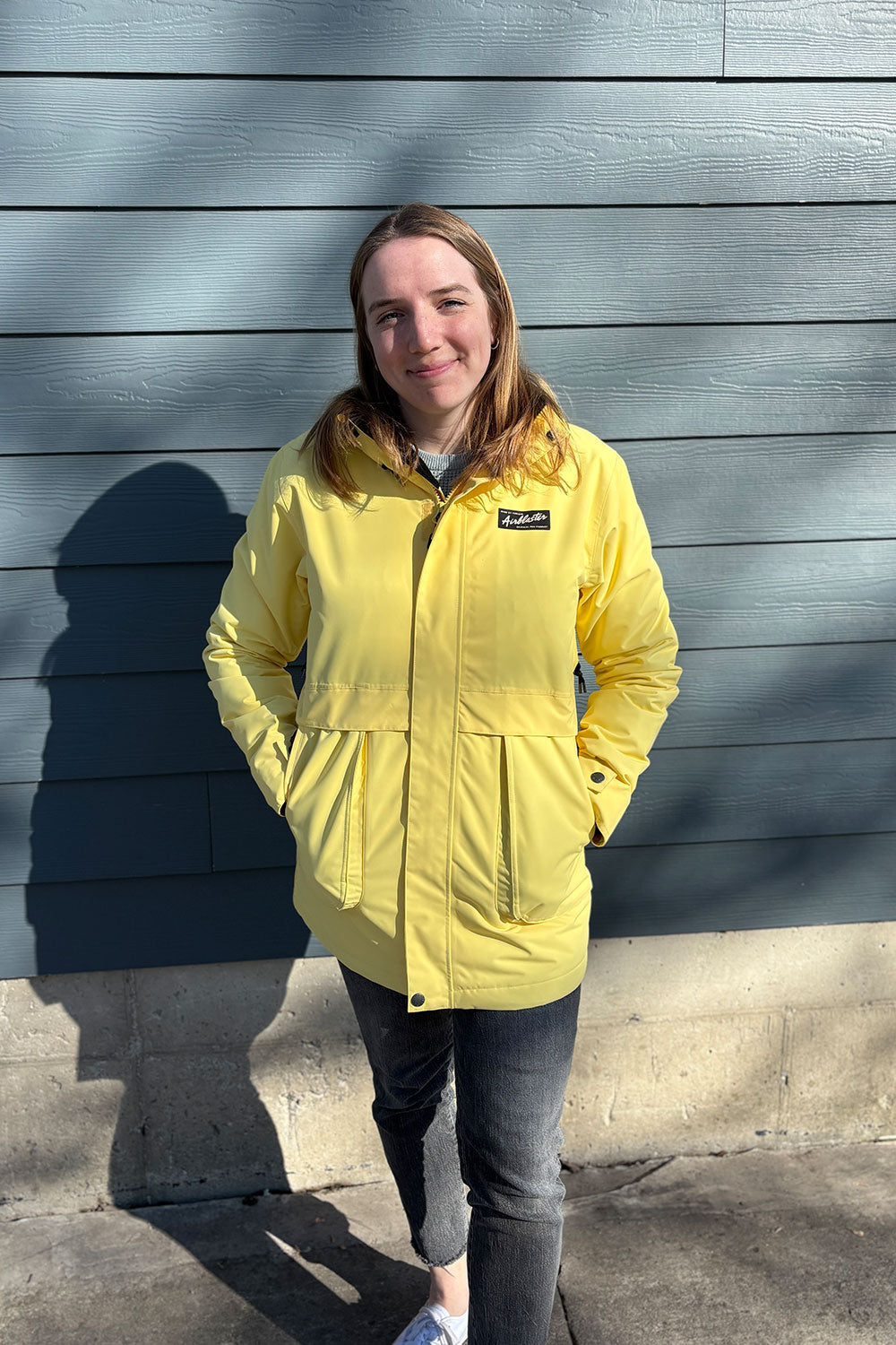 Person wearing a yellow jacket standing against a gray wall.