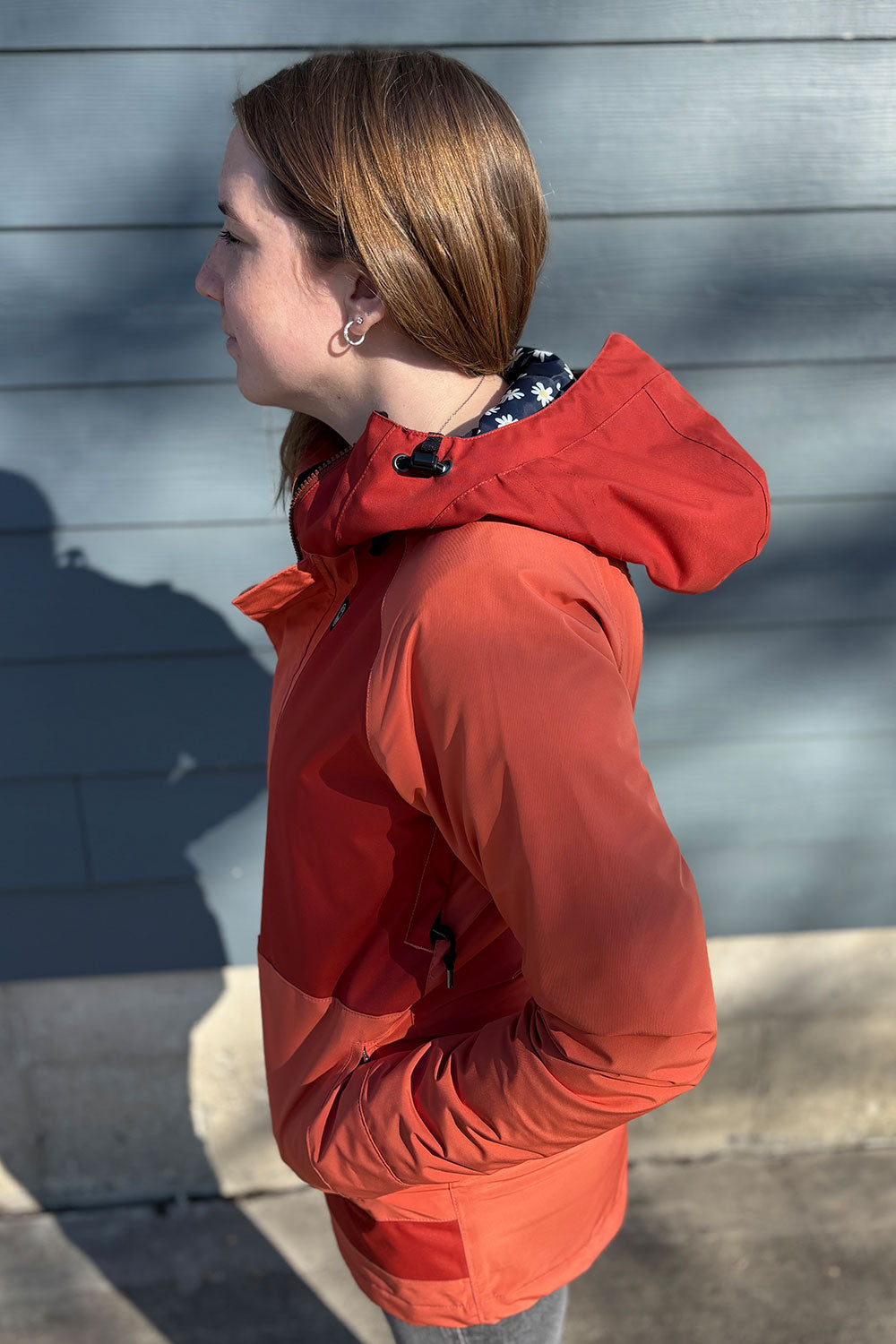 Person wearing a red jacket standing against a gray wall.