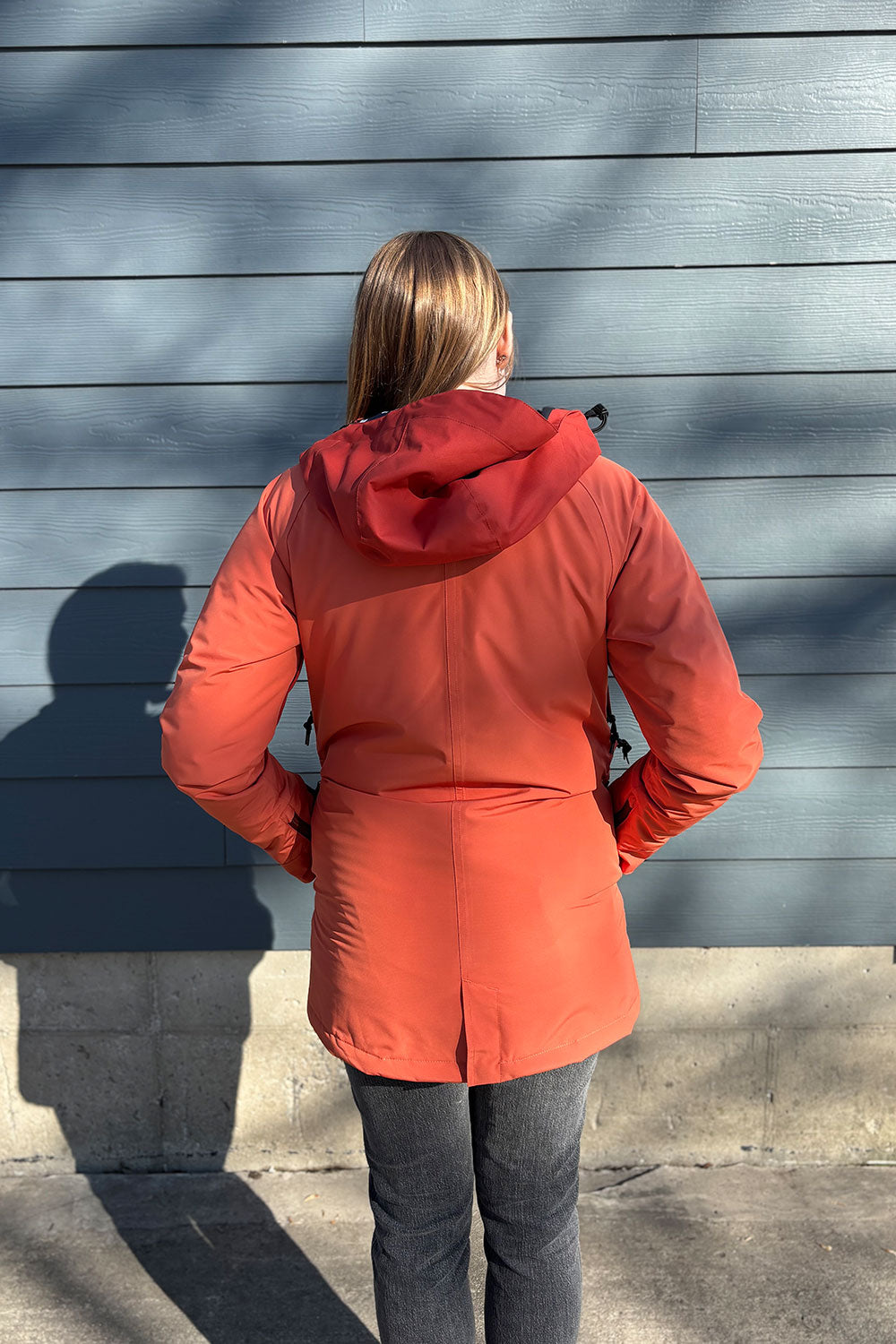 Person wearing a red coat standing against a gray wall.