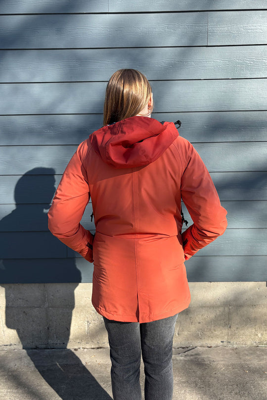 Person wearing a red coat standing against a gray wall.