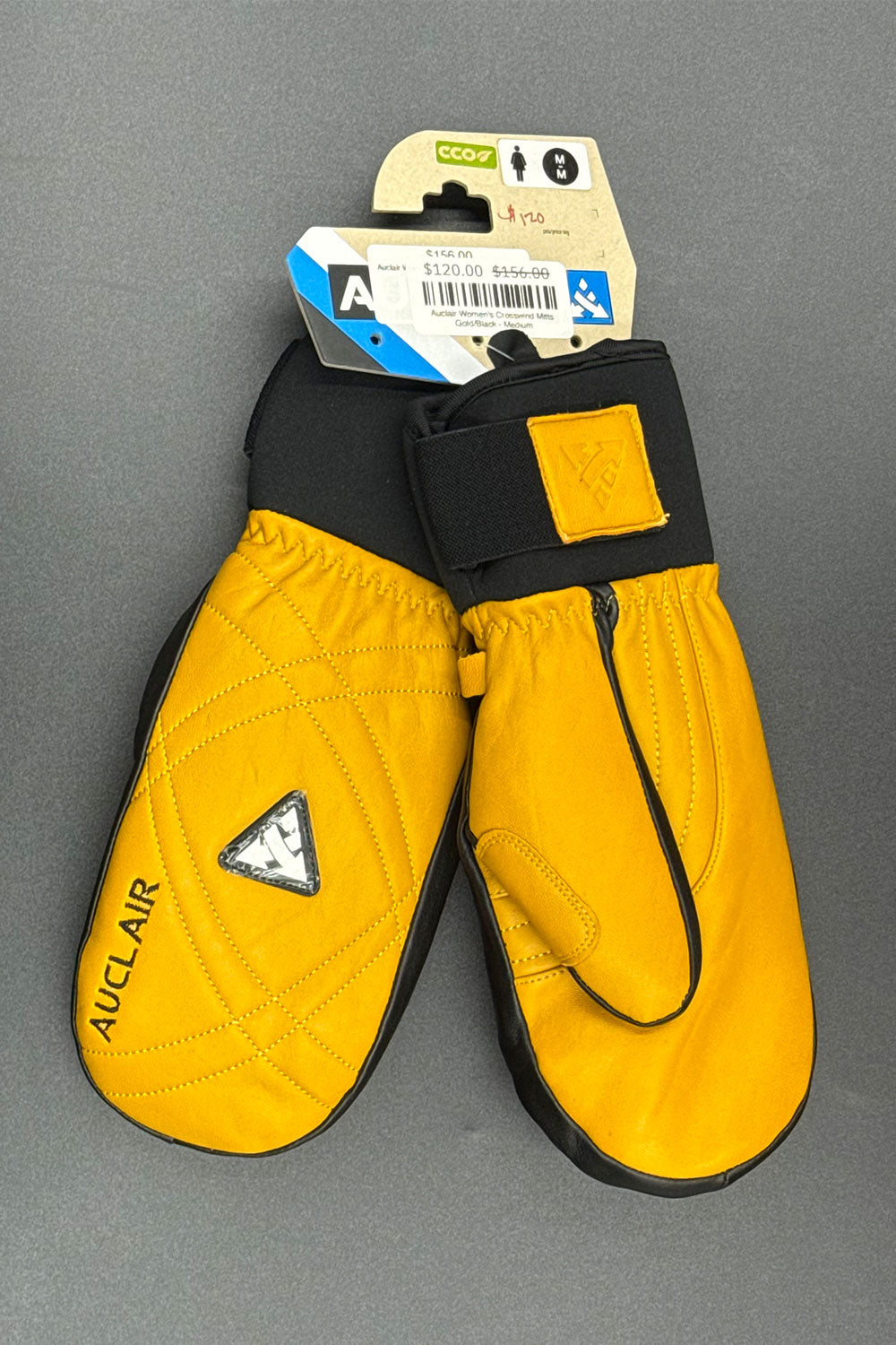 Gold leather mittens with black straps on a gray background