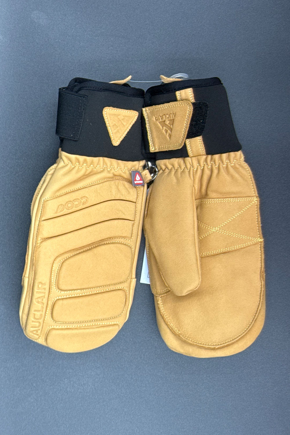 Pair of tan ski mittens with black wristbands on a blue background