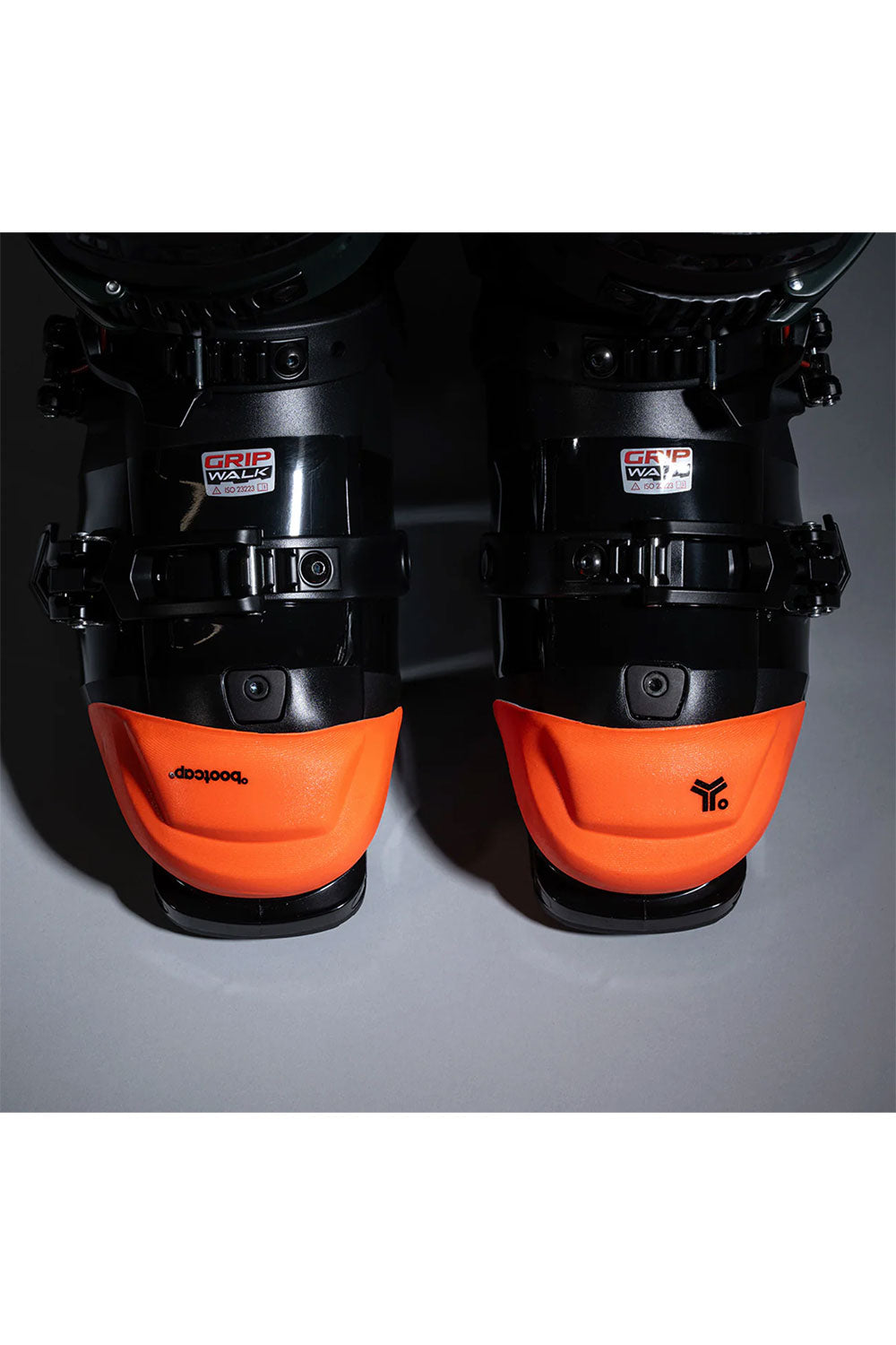 Pair of ski boots with orange soles and black shells on a gray background