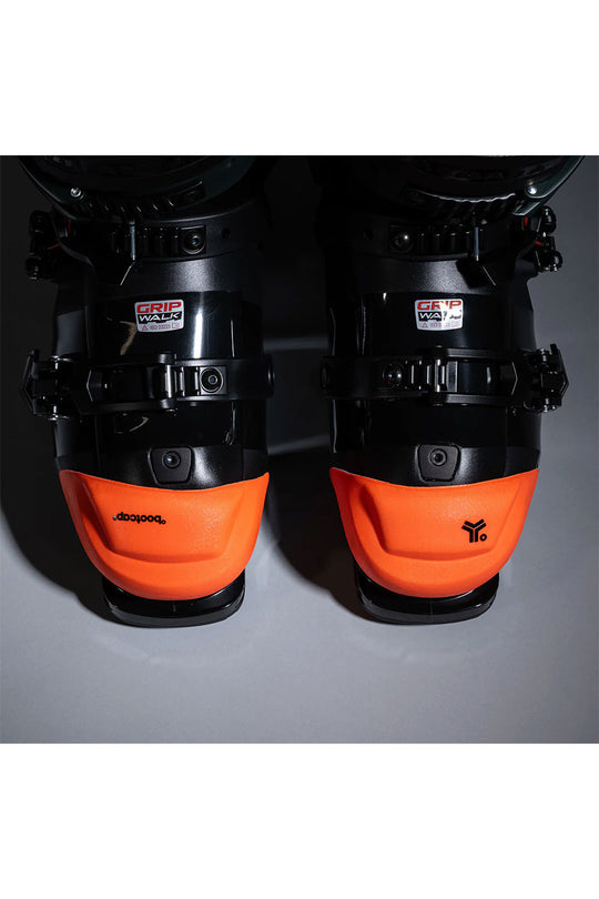 Pair of ski boots with orange soles and black shells on a gray background