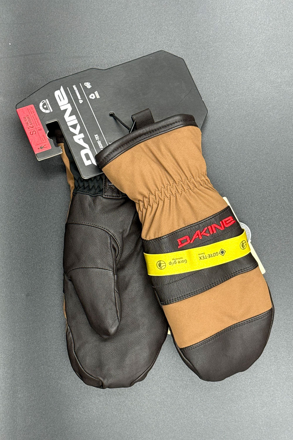 Pair of black and brown mittens with Dakine branding on a gray background