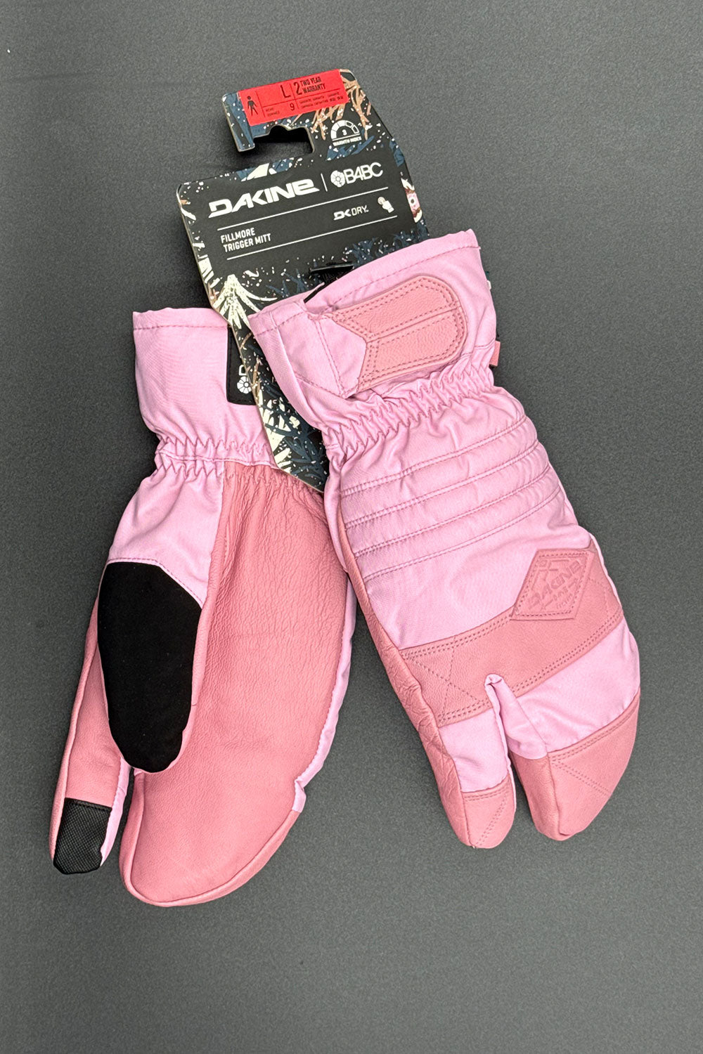 Pink gloves with black accents on a gray background, featuring a Dakine brand tag.