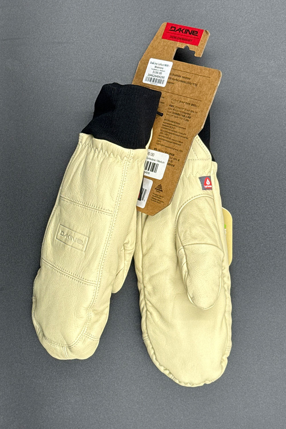Pair of beige mittens with a visible brand label on a gray background