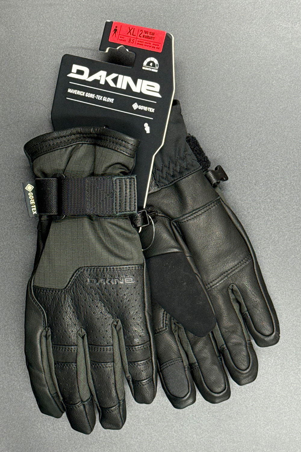 Pair of Dakine gloves with packaging on a gray background