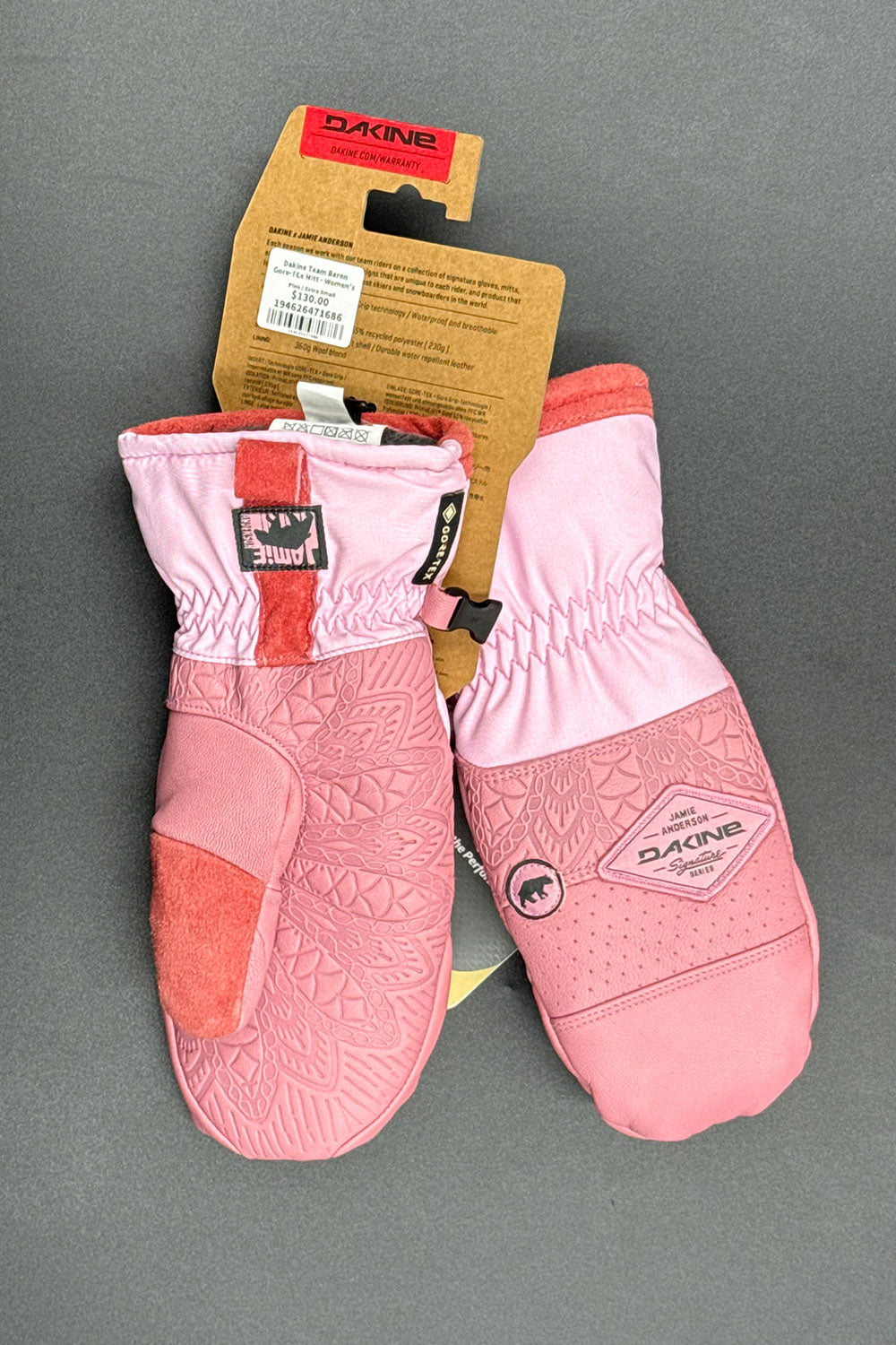 Pink mittens with red accents on a gray background, featuring a Dakine label.