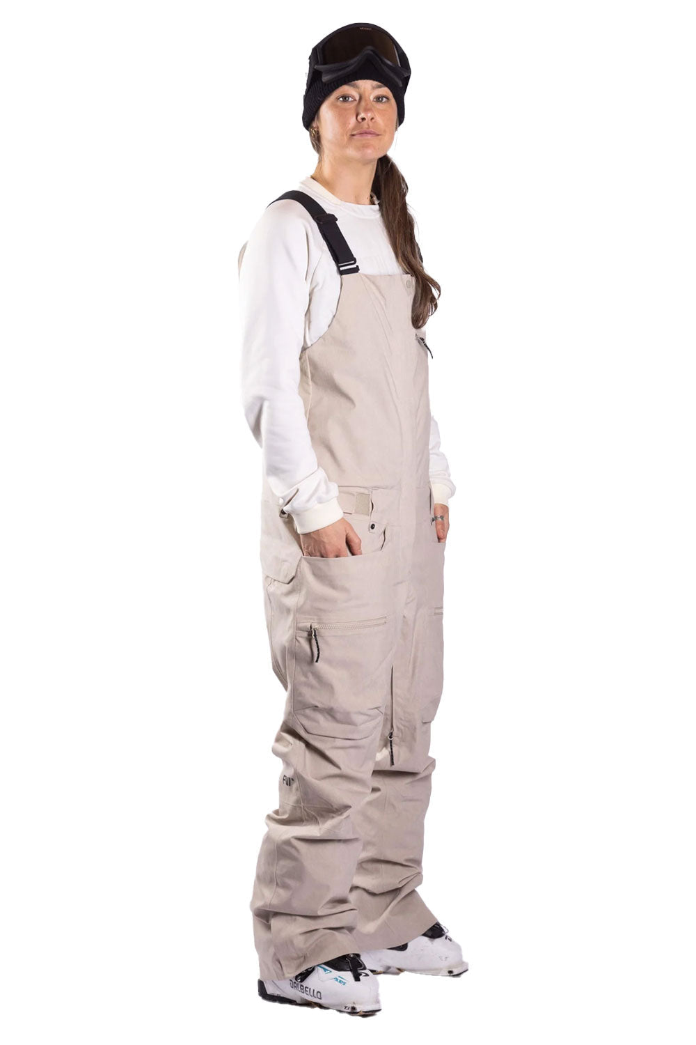 Person wearing beige bib overalls and a black beanie on a white background