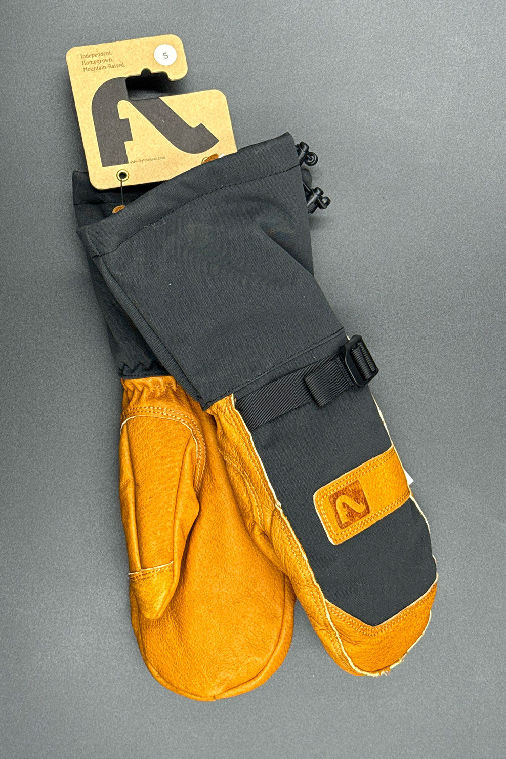 Pair of black and leather mittens with a brand tag on a gray background