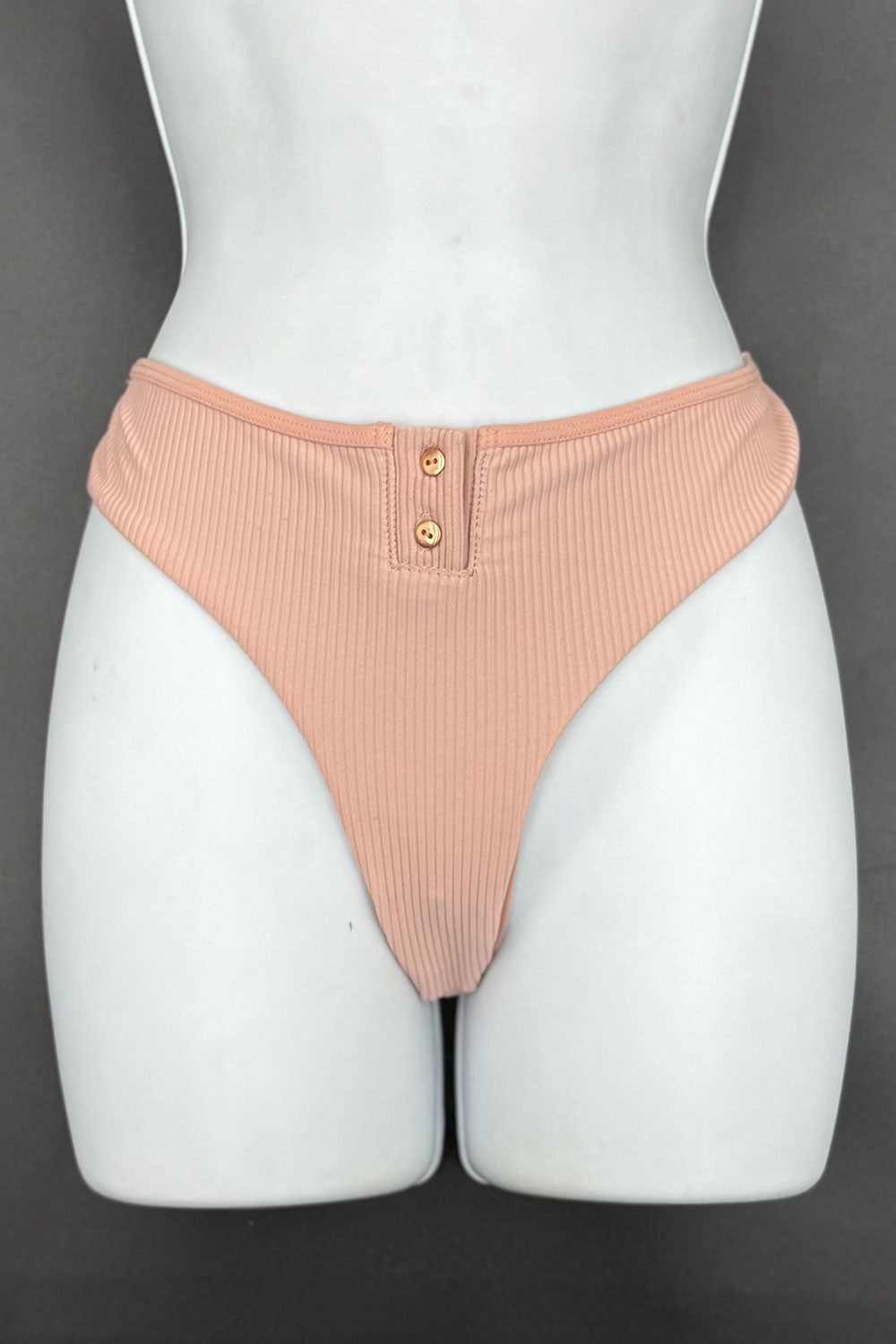 Mannequin wearing a pair of peach ribbed underwear with buttons on a dark background