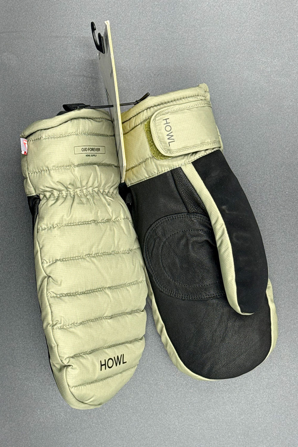 Pair of moss green mittens with 'HOWL' branding on a gray background