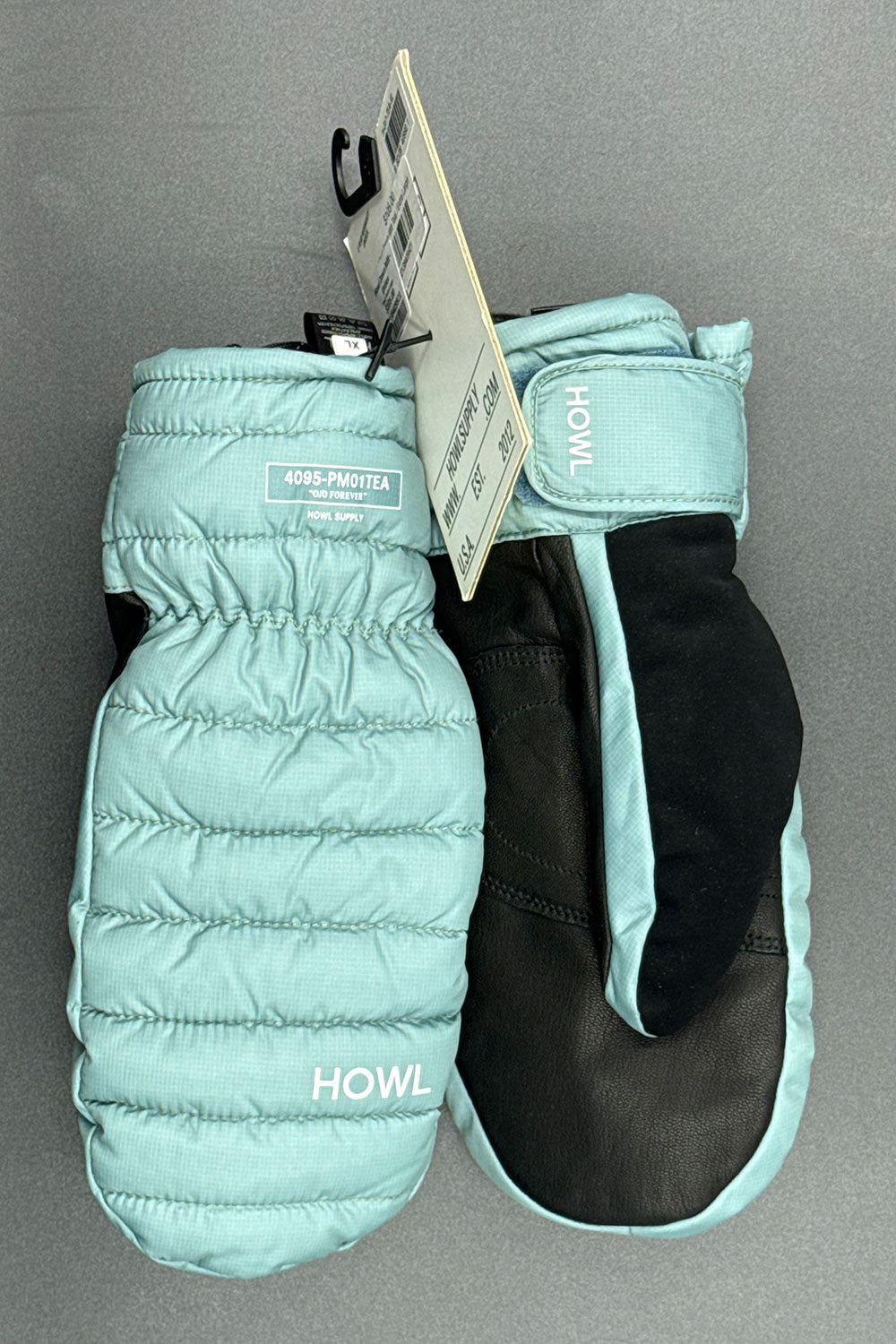 Pair of teal mittens with a black interior on a gray background, featuring the brand 'HOWL'.