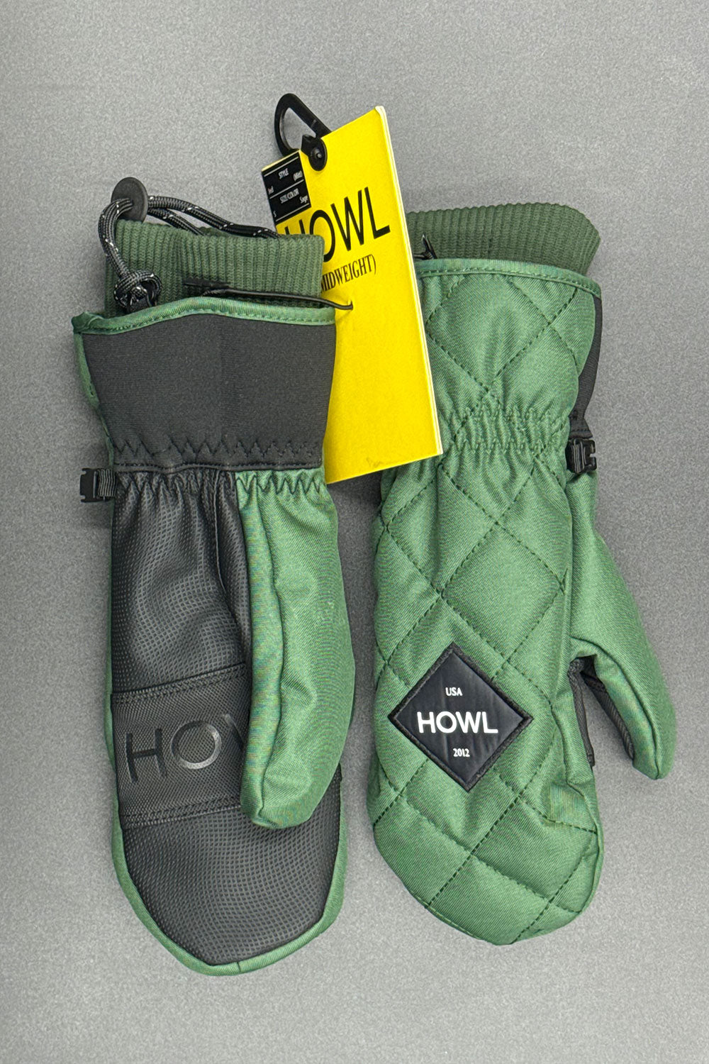 Green and black mittens with a yellow tag on a gray background