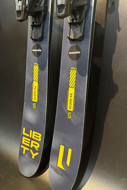 Two gray skis with yellow text and branding on a dark background