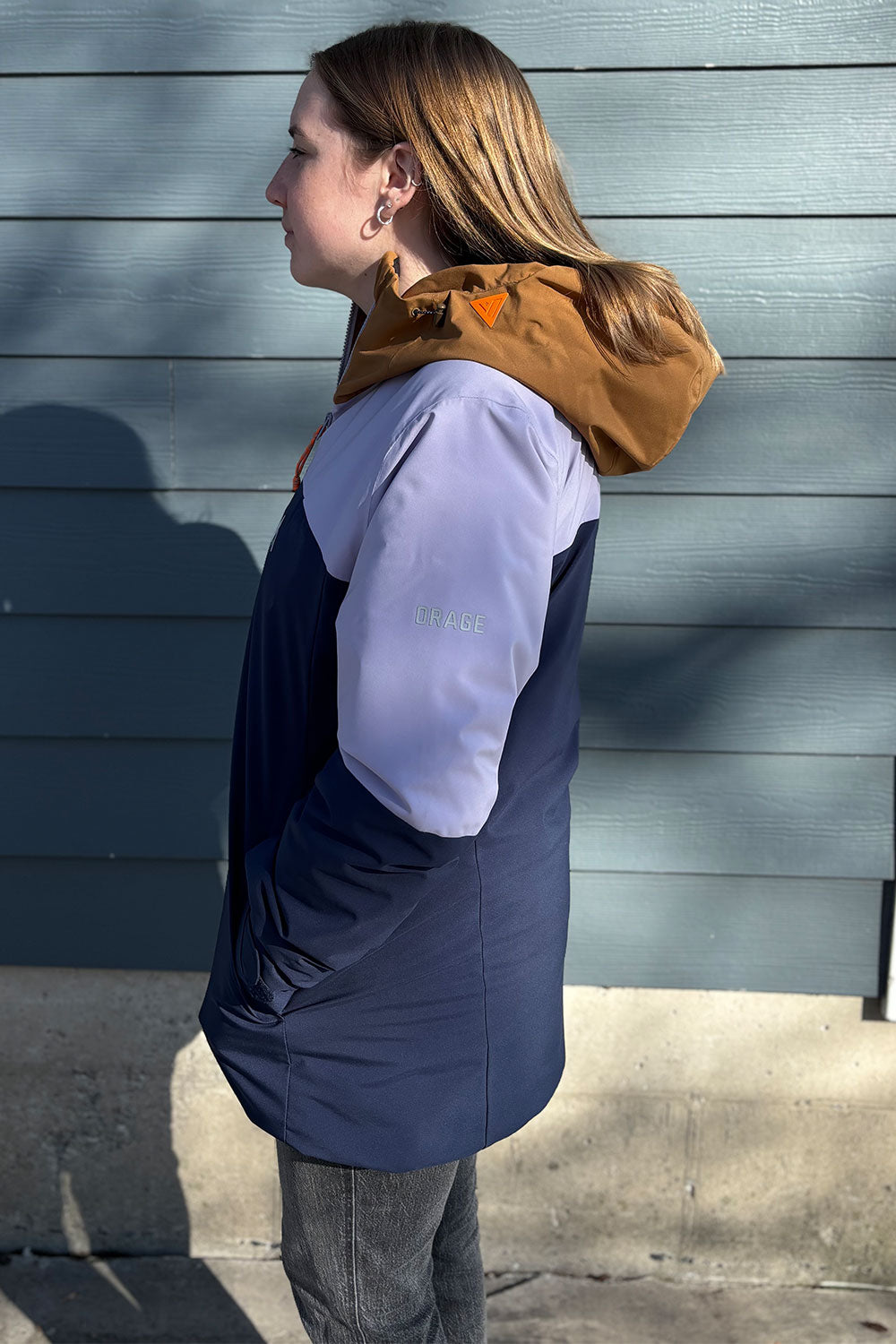 Person wearing a blue and white jacket with a brown hood against a gray wall.