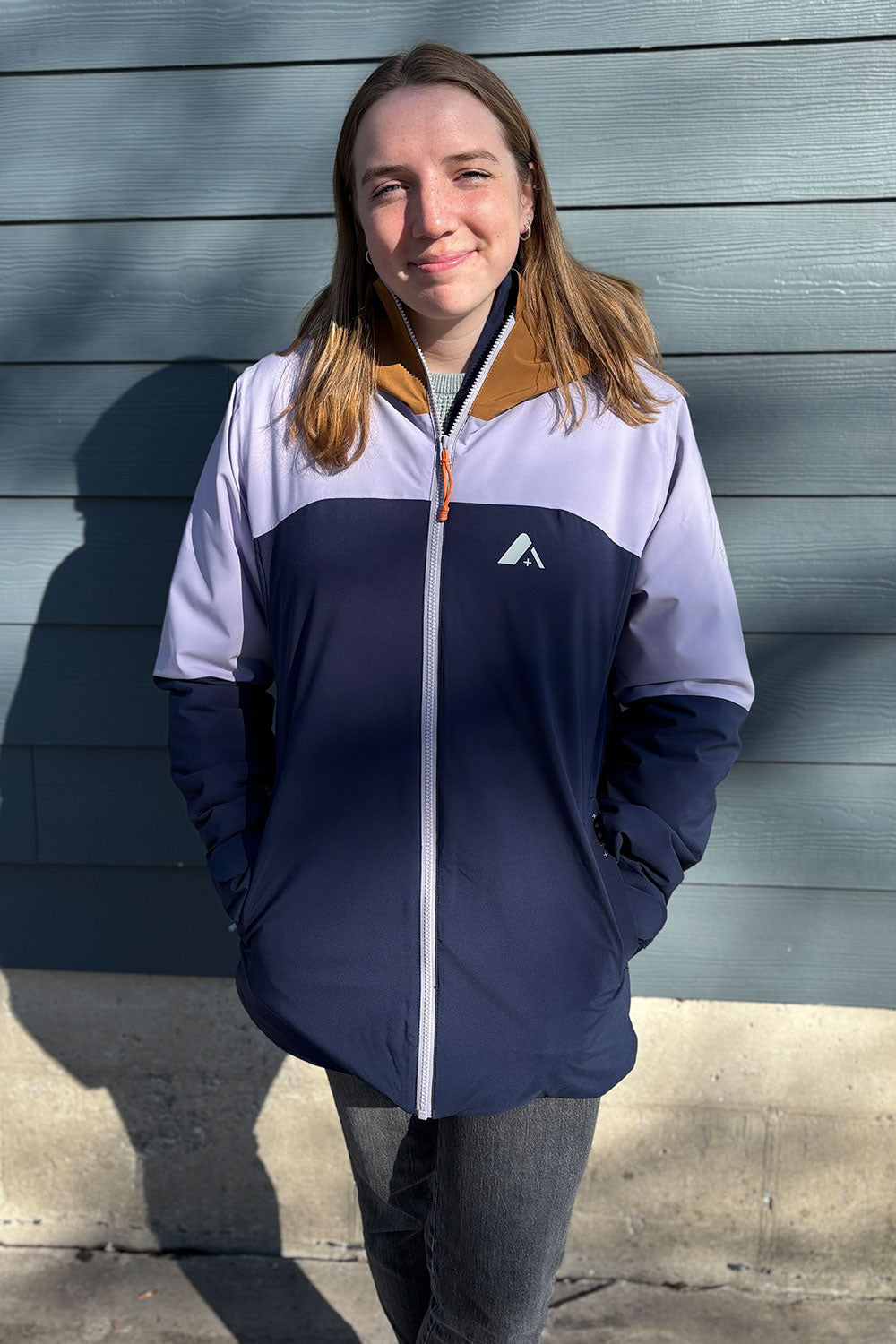 Person wearing a two-tone jacket with a logo against a gray wall.