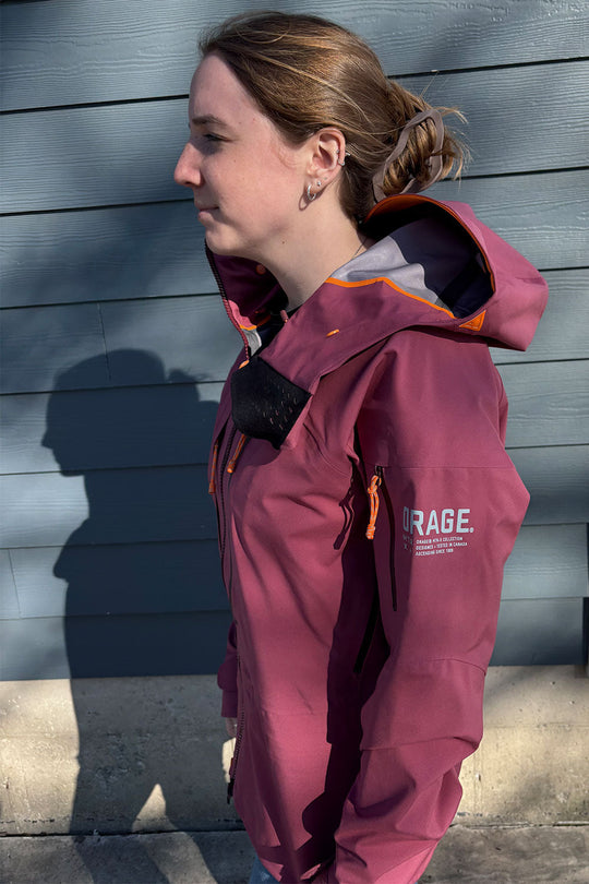 Person wearing a maroon jacket with 'Orage' branding against a gray wall.